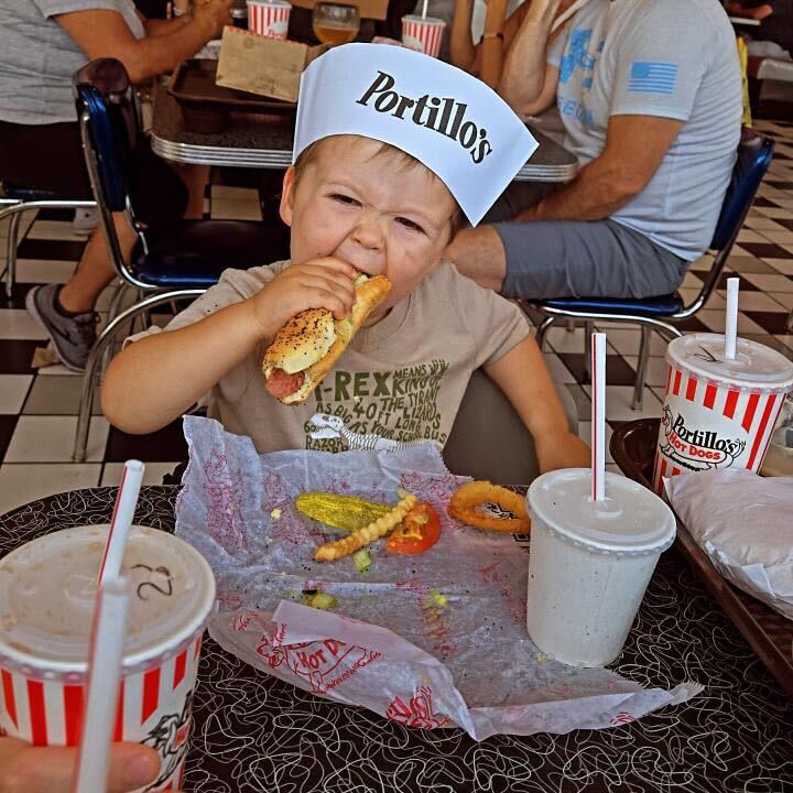 Child eating a hot dog wearing a Portillo's hat